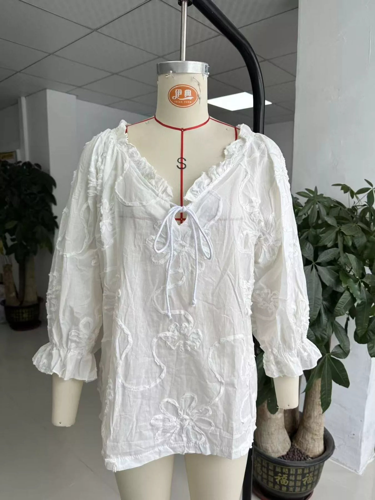 White floral embroidered tie-neck blouse on mannequin, ruffled neckline and sleeves