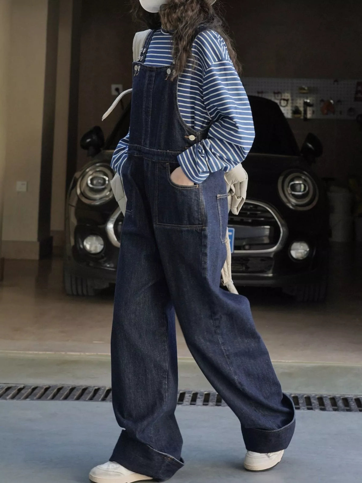 Dark-wash denim overalls on model, side view with front pockets and wide leg fit