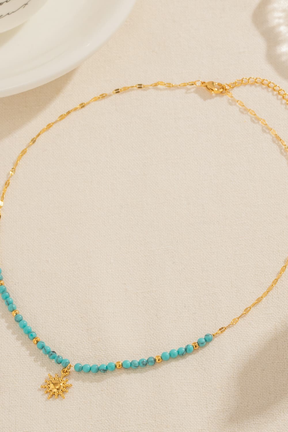 Turquoise beaded gold link necklace with sun pendant charm, laid flat