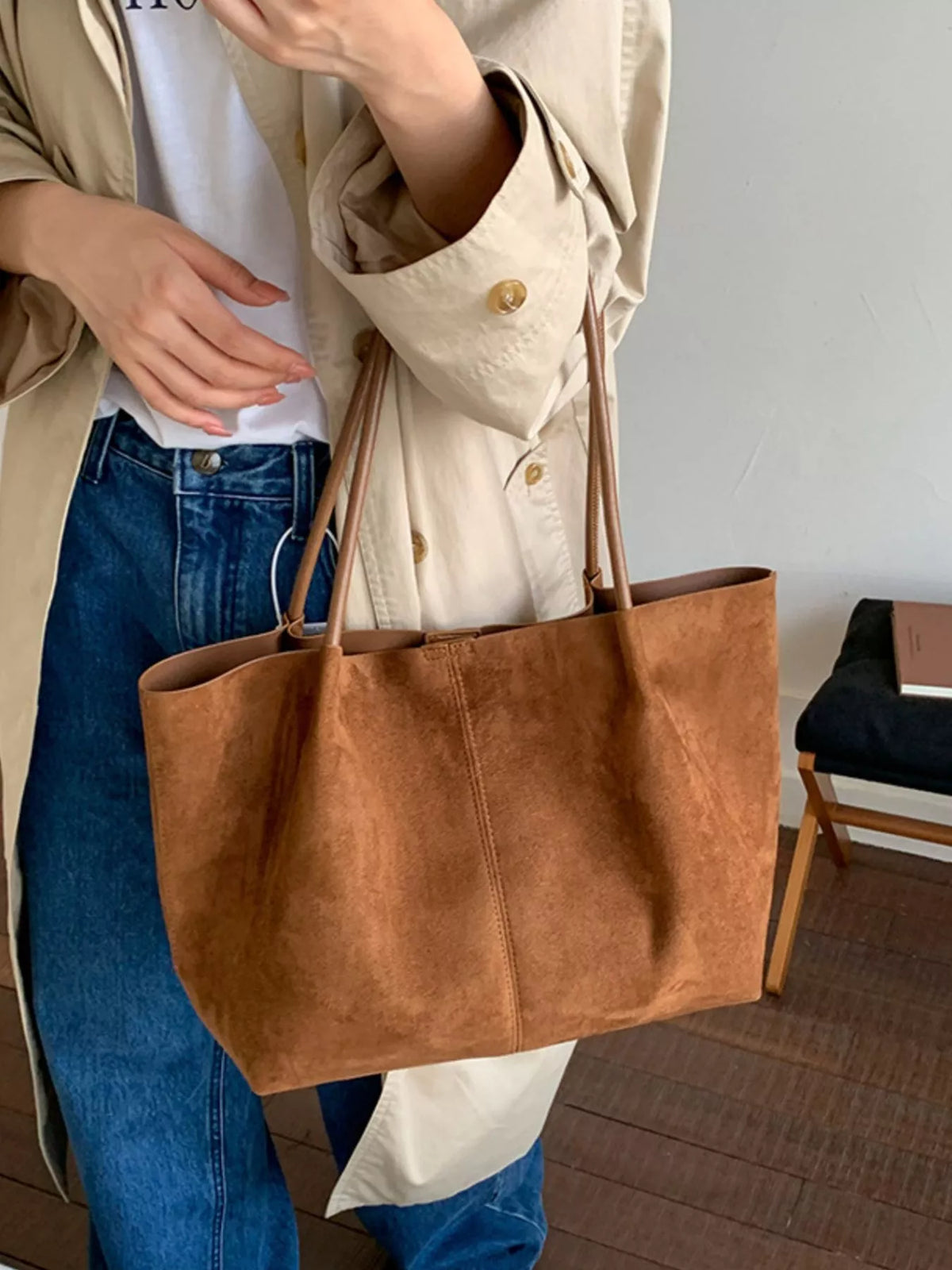 Brown suede large tote bag with open top and double handles held by hand