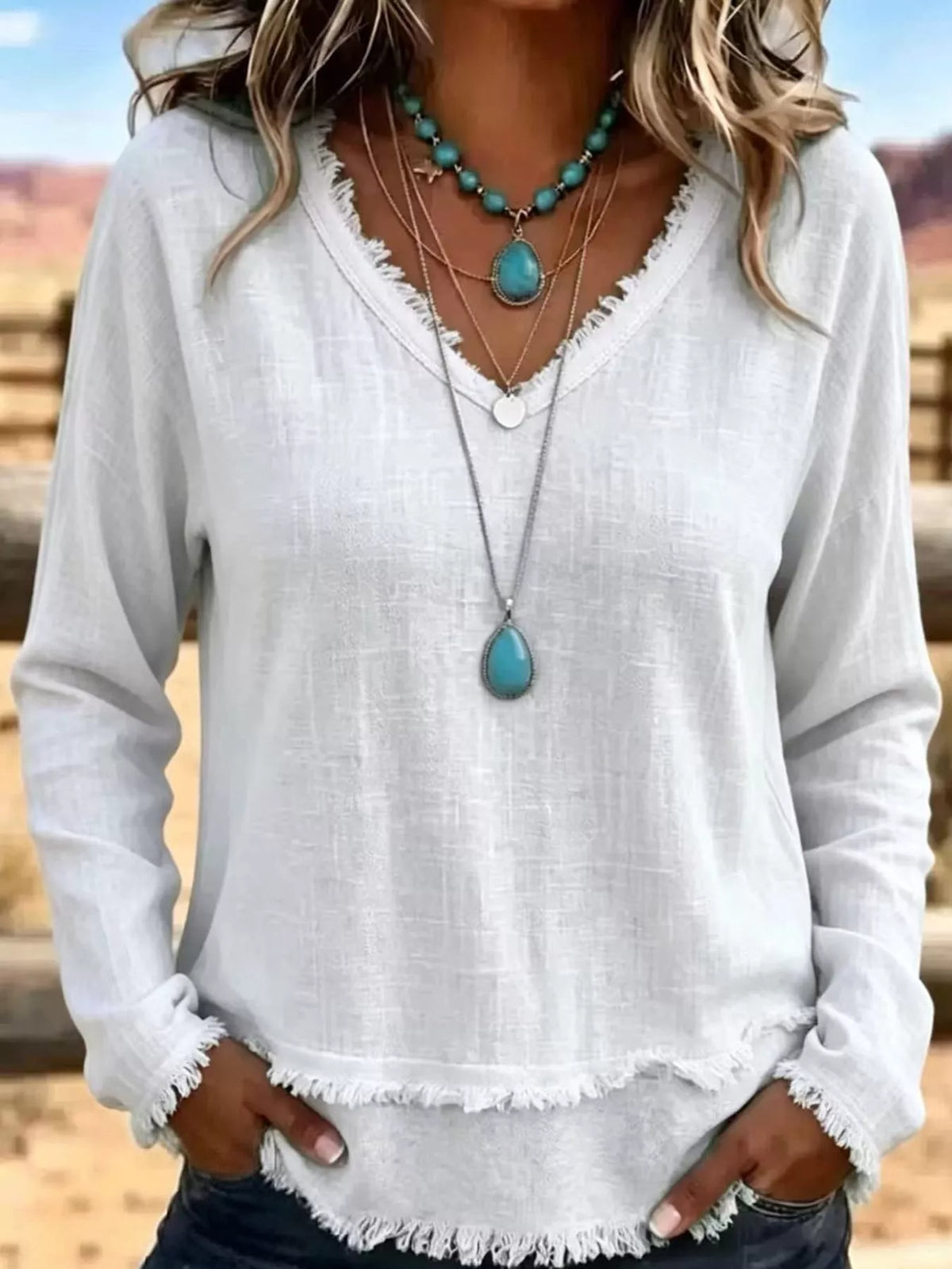 White linen V-neck blouse with frayed hem and relaxed fit, long sleeves