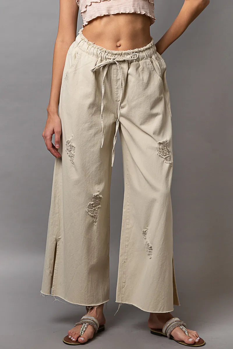 Cream distressed wide-leg drawstring pants with side slit and frayed hem