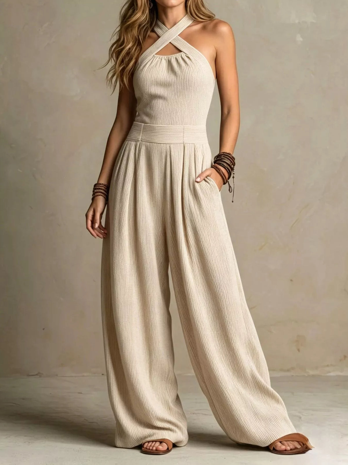 Beige halter-neck wide-leg jumpsuit with sleeveless halter straps and gathered waist.