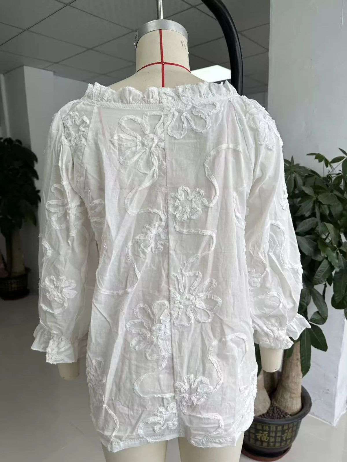 White floral embroidered blouse on mannequin, buttonless tie-neck and puff sleeves