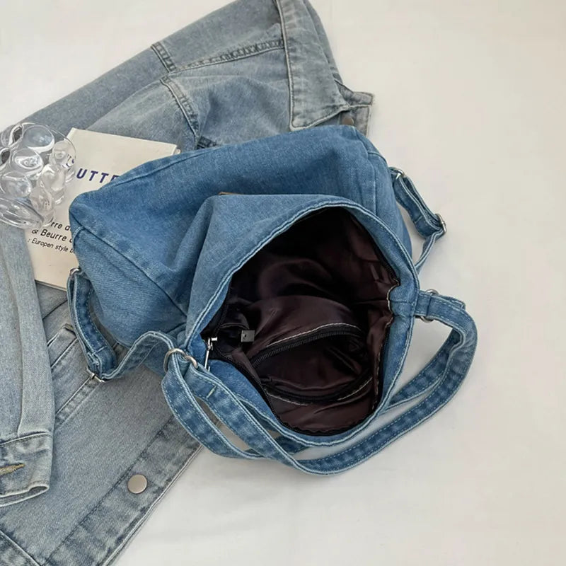 Open denim shoulder bag with adjustable strap, blue lining visible, brown front patch
