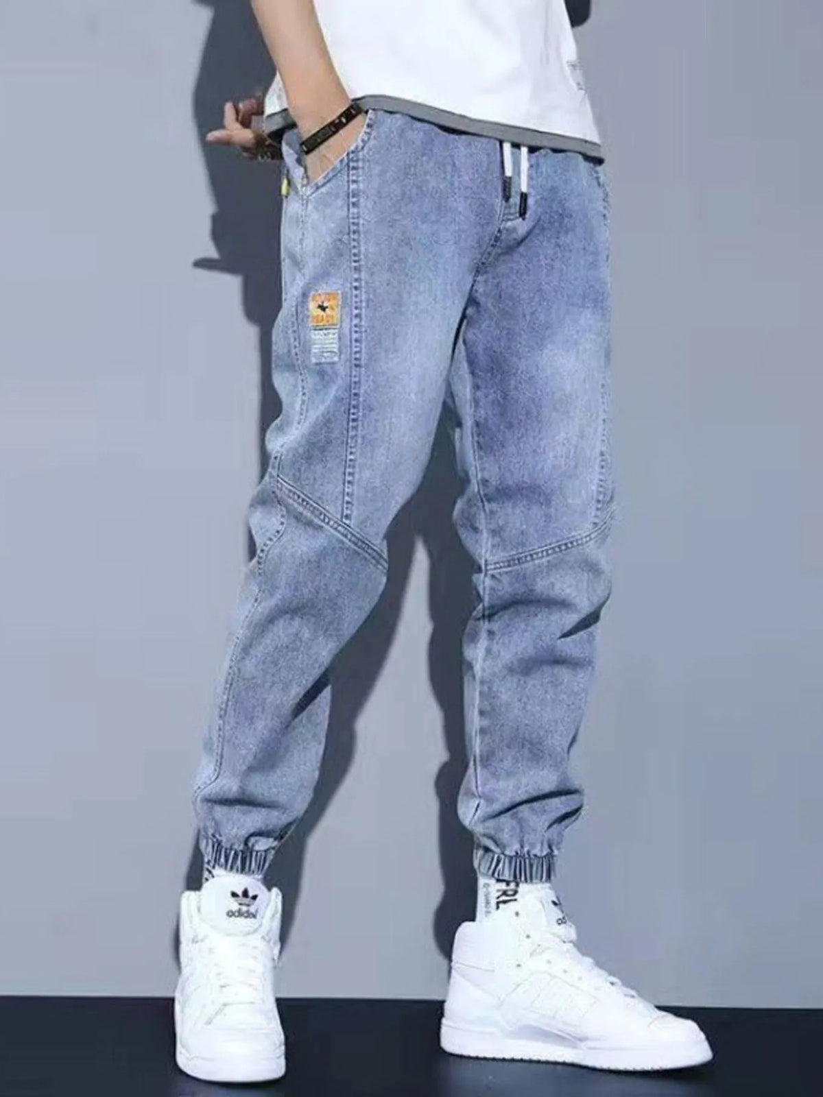 Men's washed blue drawstring jeans with pockets and cuffed jogger hems.