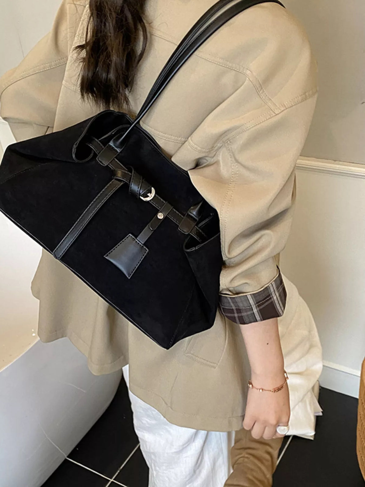 Black suede shoulder bag with buckle strap, front patch detail, and metal rings