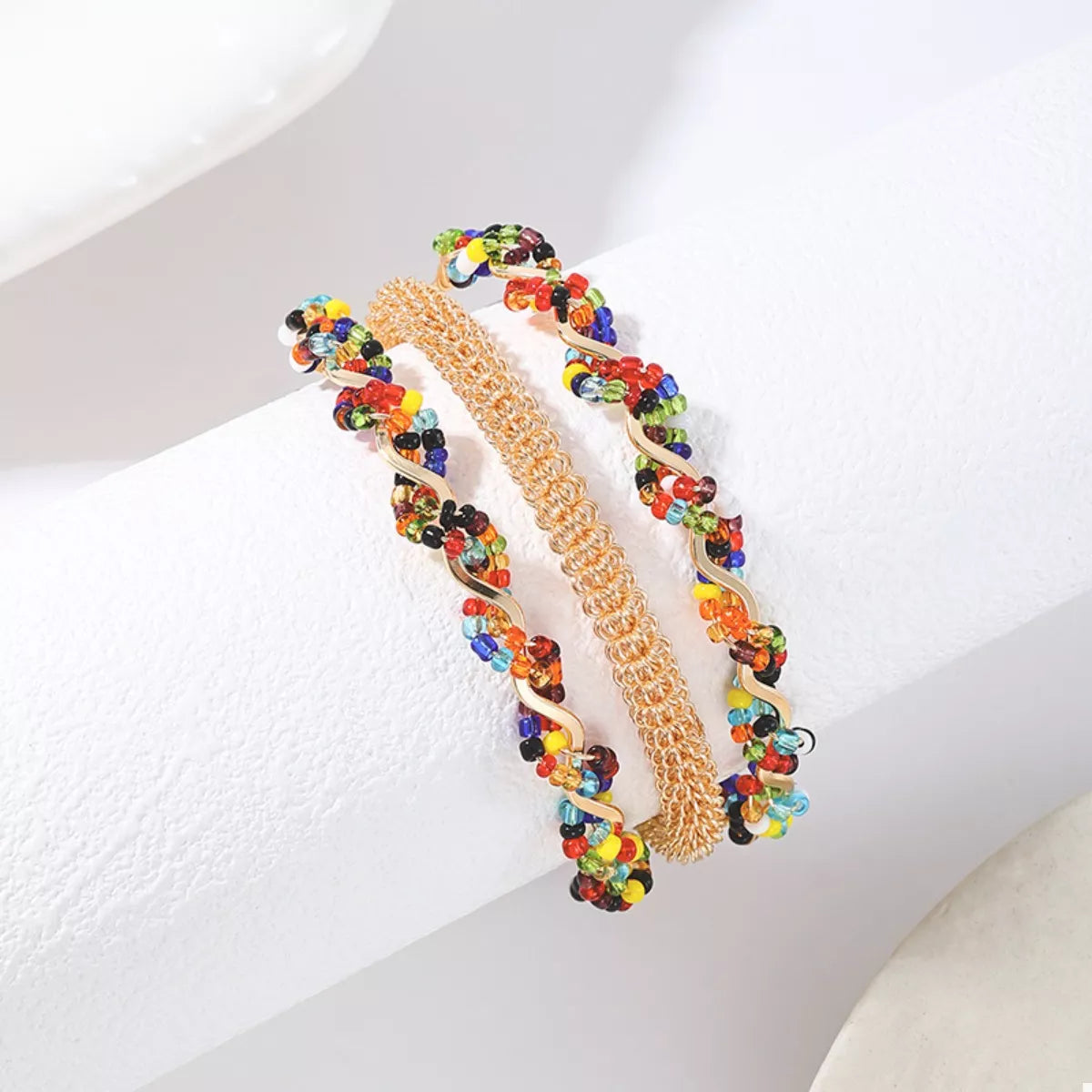 Three-layer gold-tone beaded open bracelet on forearm, multicolor accents