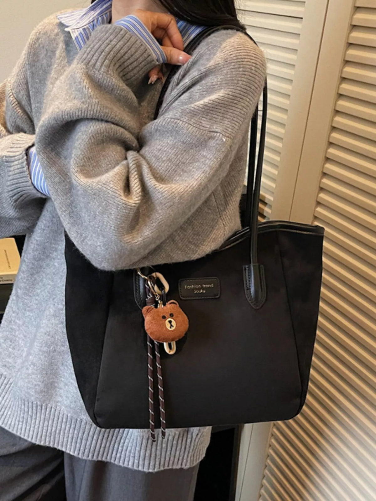 Black suede tote bag with long handles, zipper top, and bear keychain charm