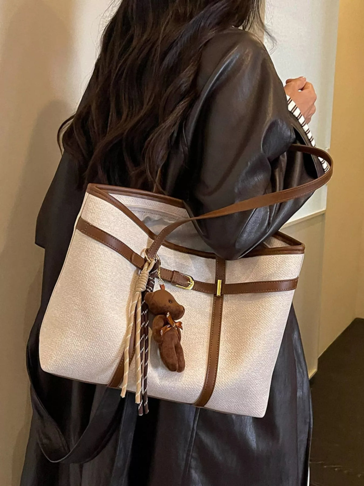 Off-white vegan leather tote bag with brown trim and teddy keychain on hanging tassel