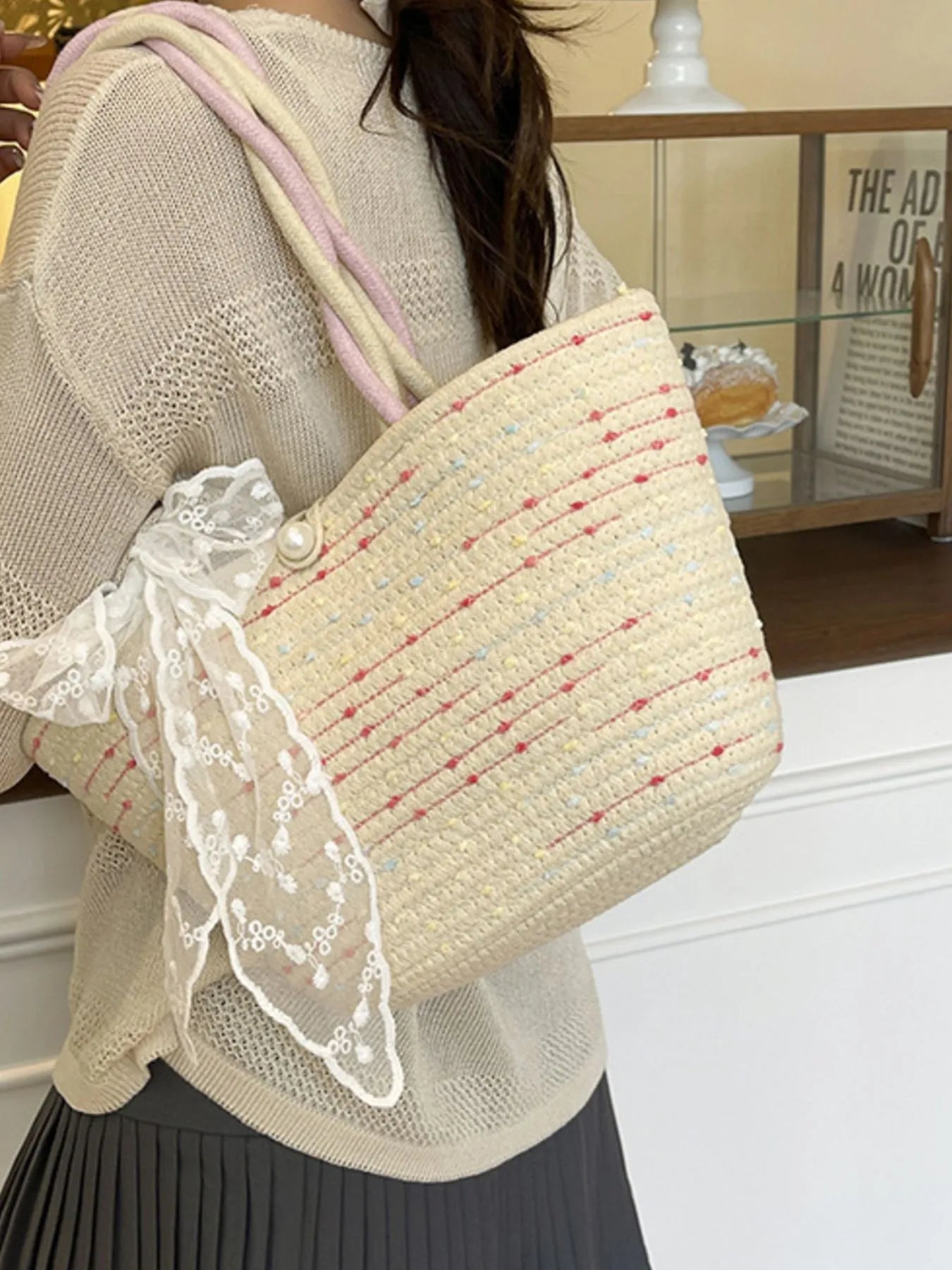 Woven straw shoulder bag worn on shoulder, with white lace trim and pink handles