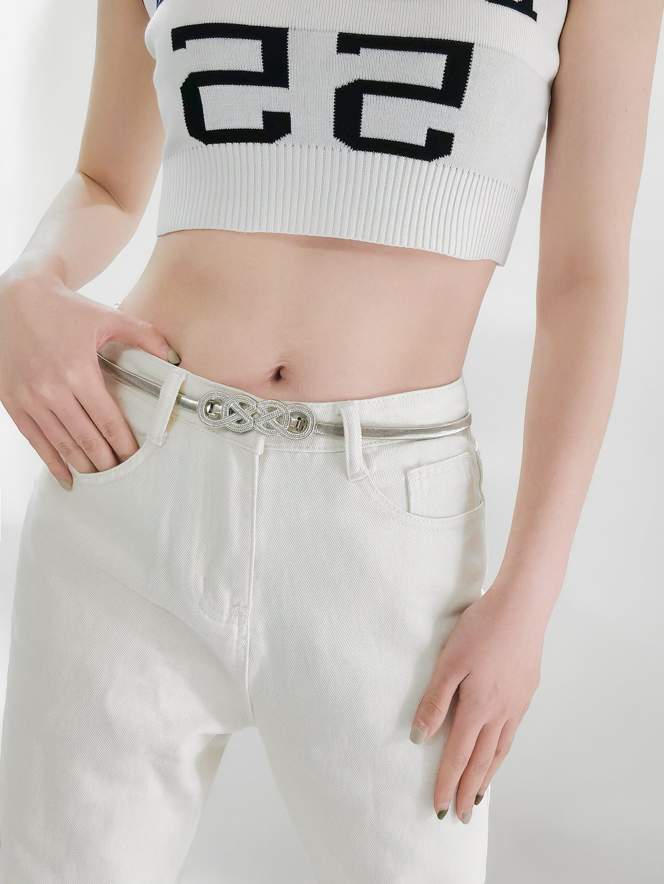 White jeans with gold-tone knot buckle belt at waistband, close-up view