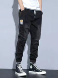 Men's washed black drawstring jeans with pockets and cuffed jogger hems.