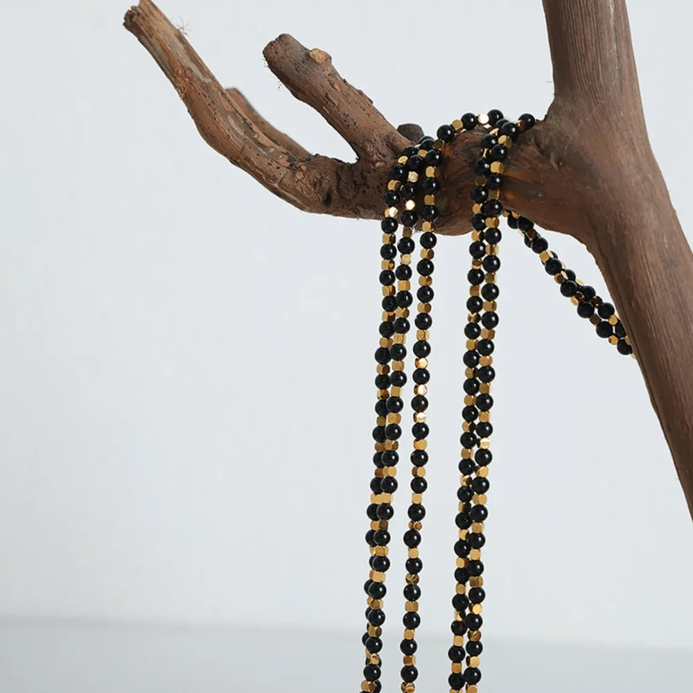 Agate beaded necklace hanging from wood, layered black beads with gold-tone accents