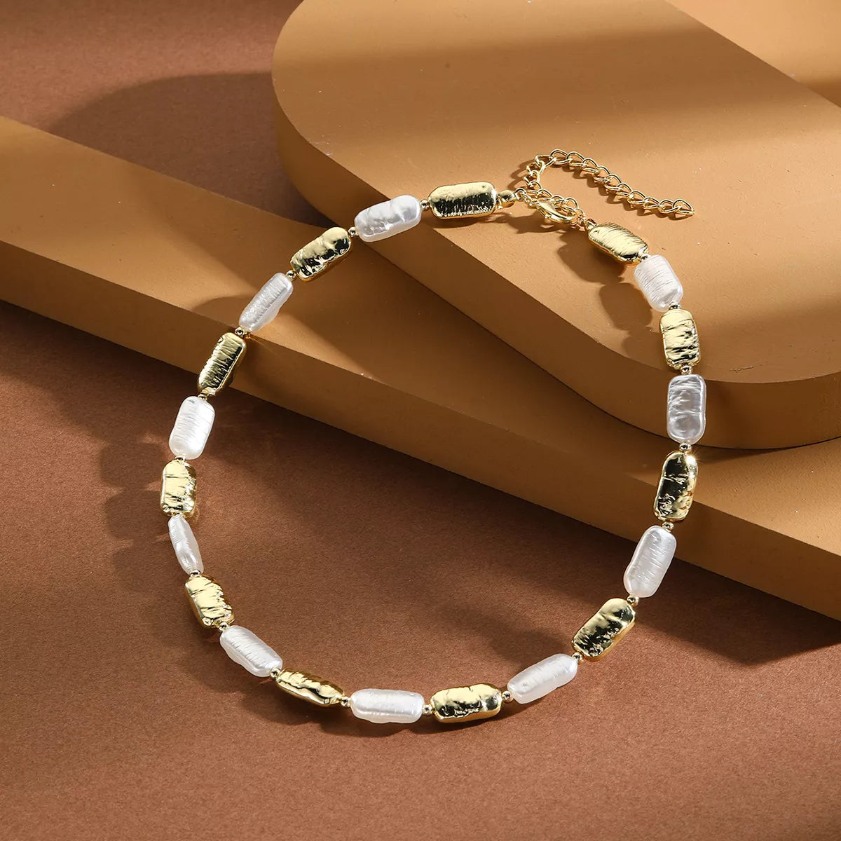 Pearl chain necklace with white pearl beads and gold-tone spacers, shown on a stand