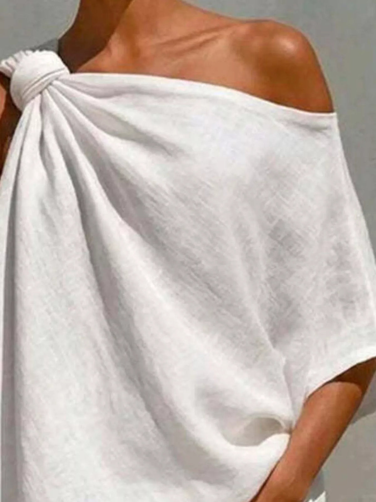 White one-shoulder blouse close-up with knotted shoulder and flowing draped fabric