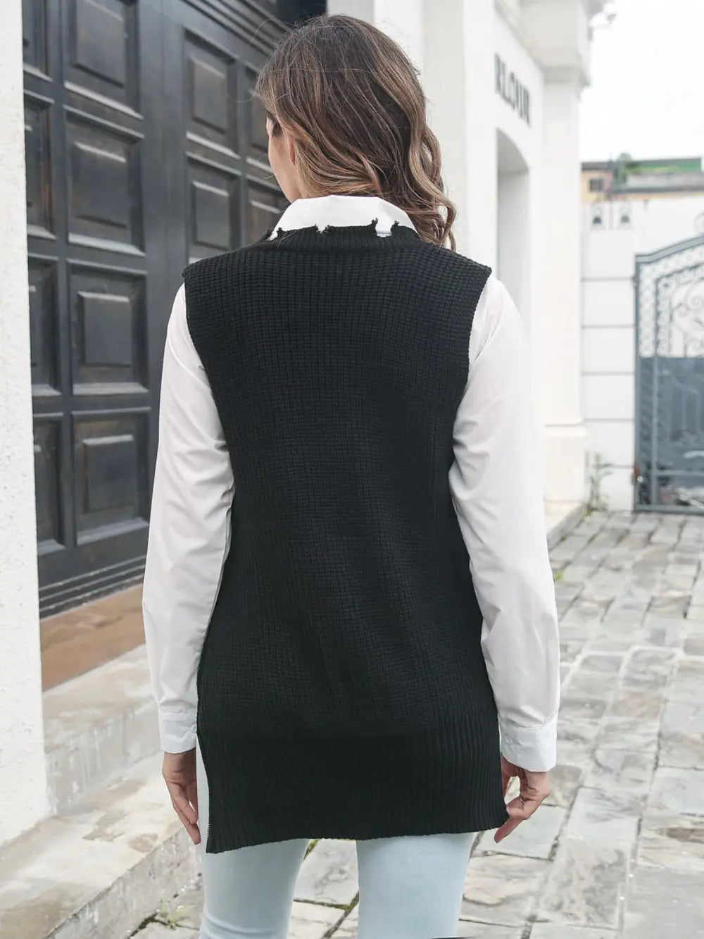 Black knit sweater vest back view with frayed split hem, over white shirt sleeves