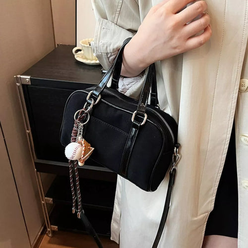 Black crossbody handbag with top handles, buckle strap and dangling charm