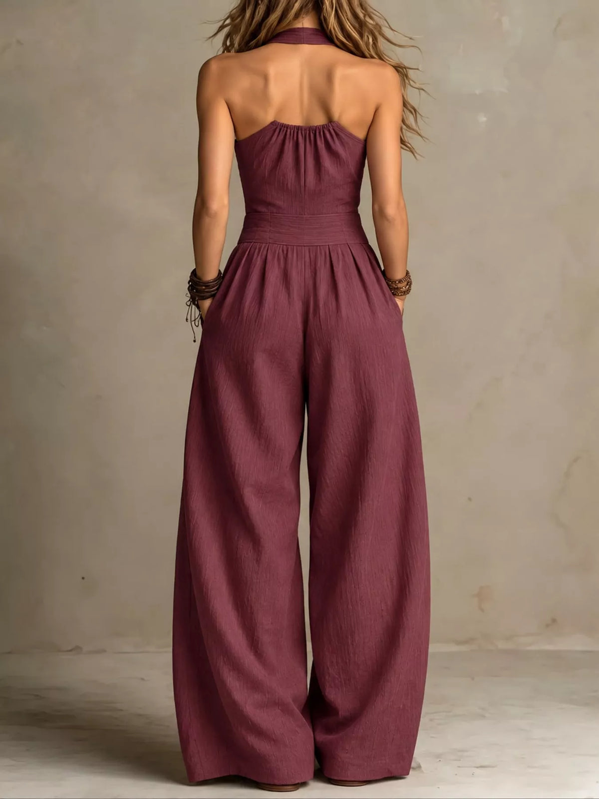 Burgundy linen jumpsuit from back view with halter strap and wide-leg trousers