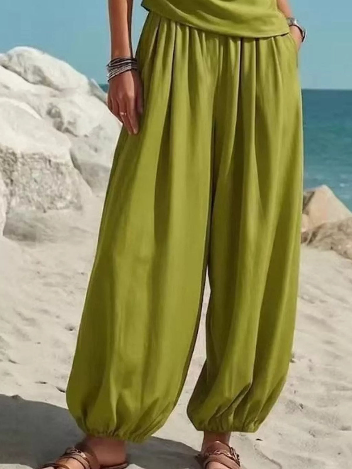 Green harem pants with gathered waist and relaxed wide legs, paired with one-shoulder top