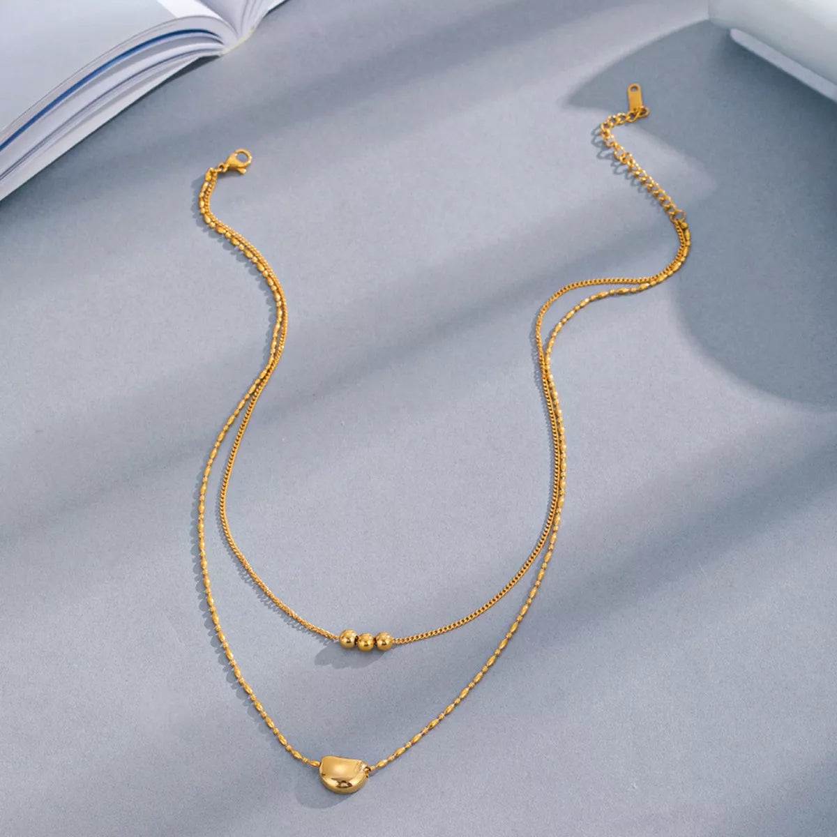 Gold double-layer necklace with heart charm, beaded center detail, and adjustable clasp.