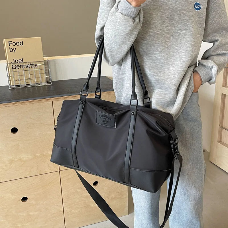 Black polyester travel duffel bag with detachable crossbody strap and front logo patch