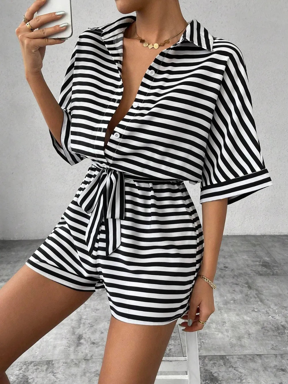 Black and white striped button-front romper with tie waist, V neckline, and cuffed sleeves