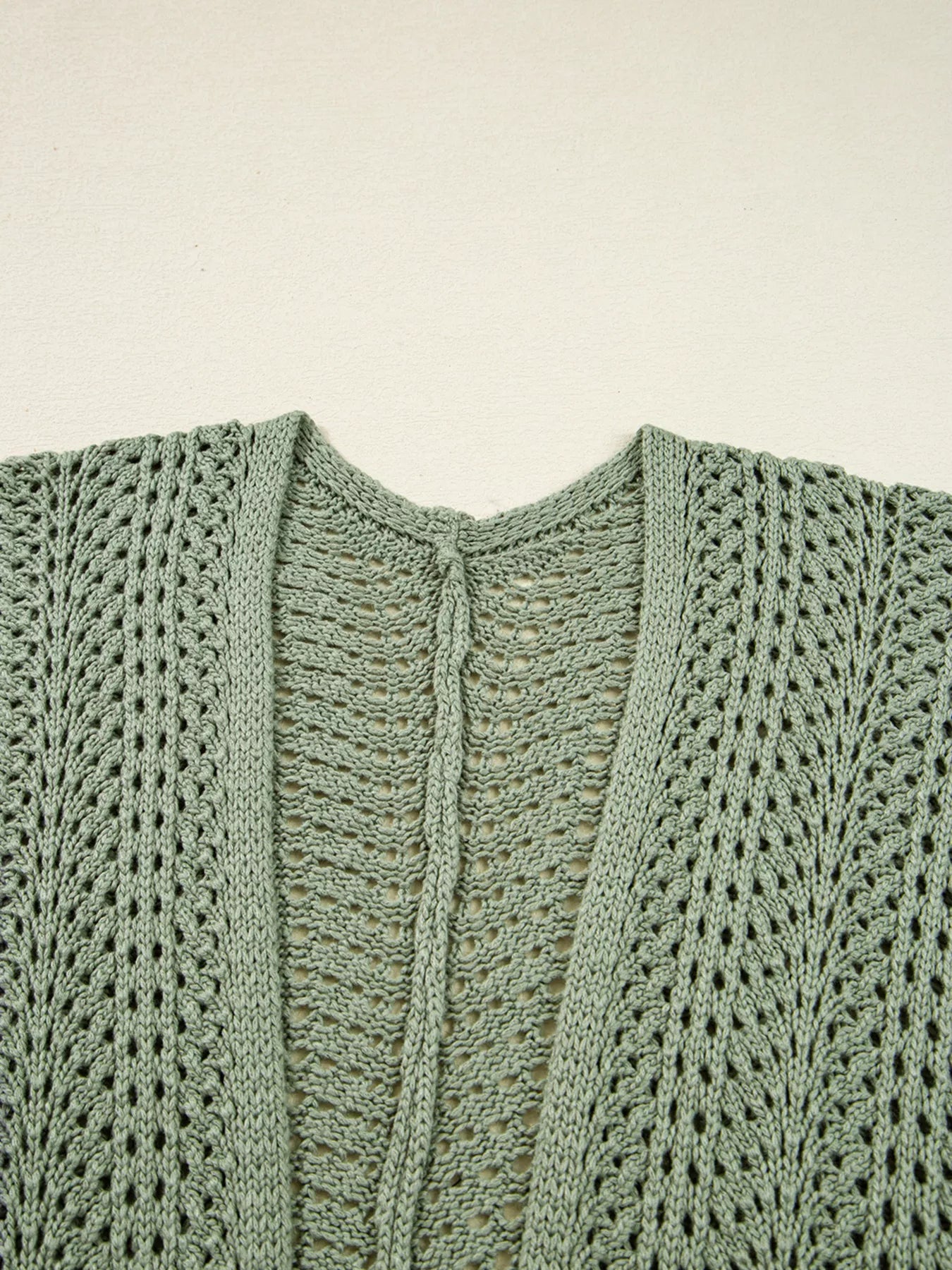 Sage eyelet knit cardigan with V-neck and center scalloped trim detail, close-up.