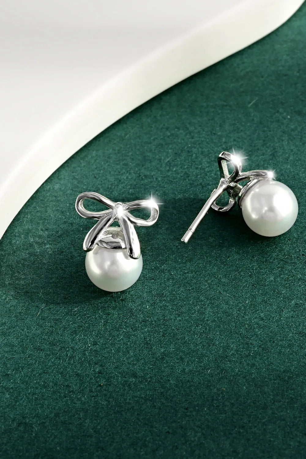 Silver bow stud earrings with round pearl drops, polished metal hardware.
