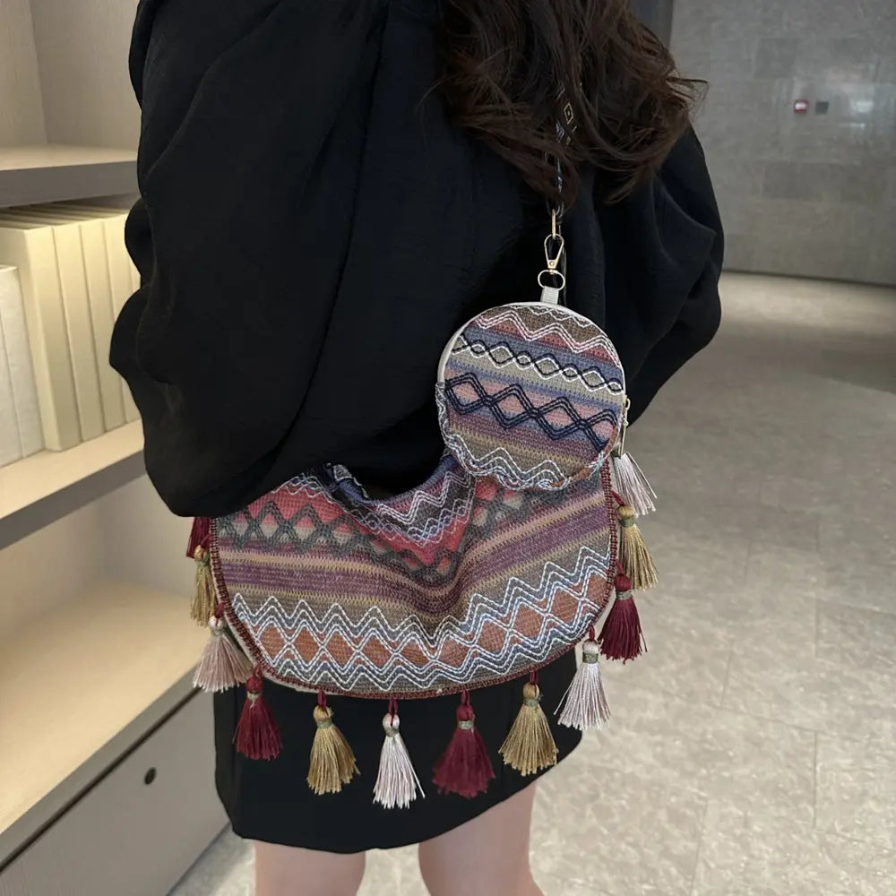 Printed crossbody bag with layered zigzag pattern, tassels, and zipper pocket.