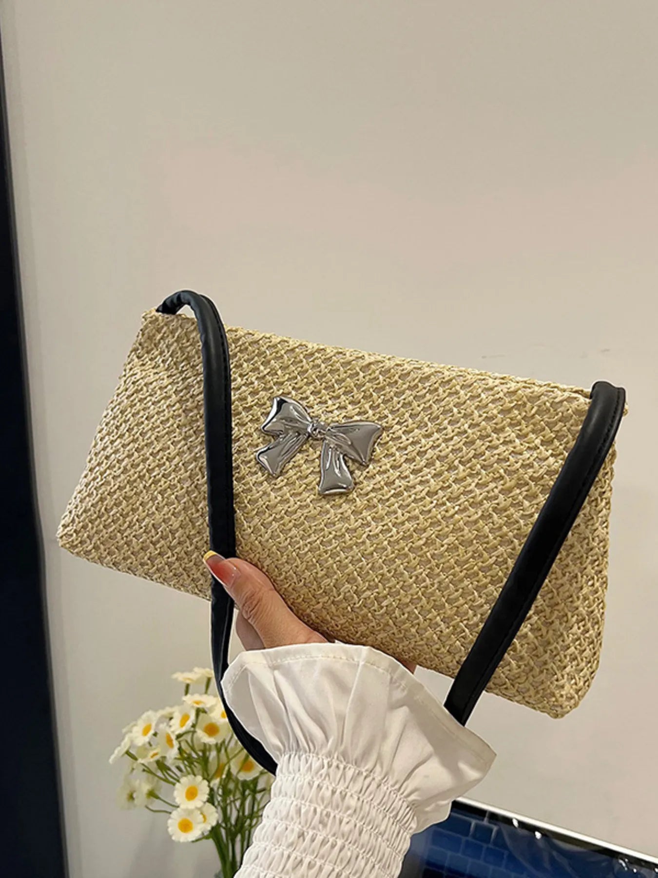 Woven straw shoulder bag with silver bow detail and black straps, tan woven texture