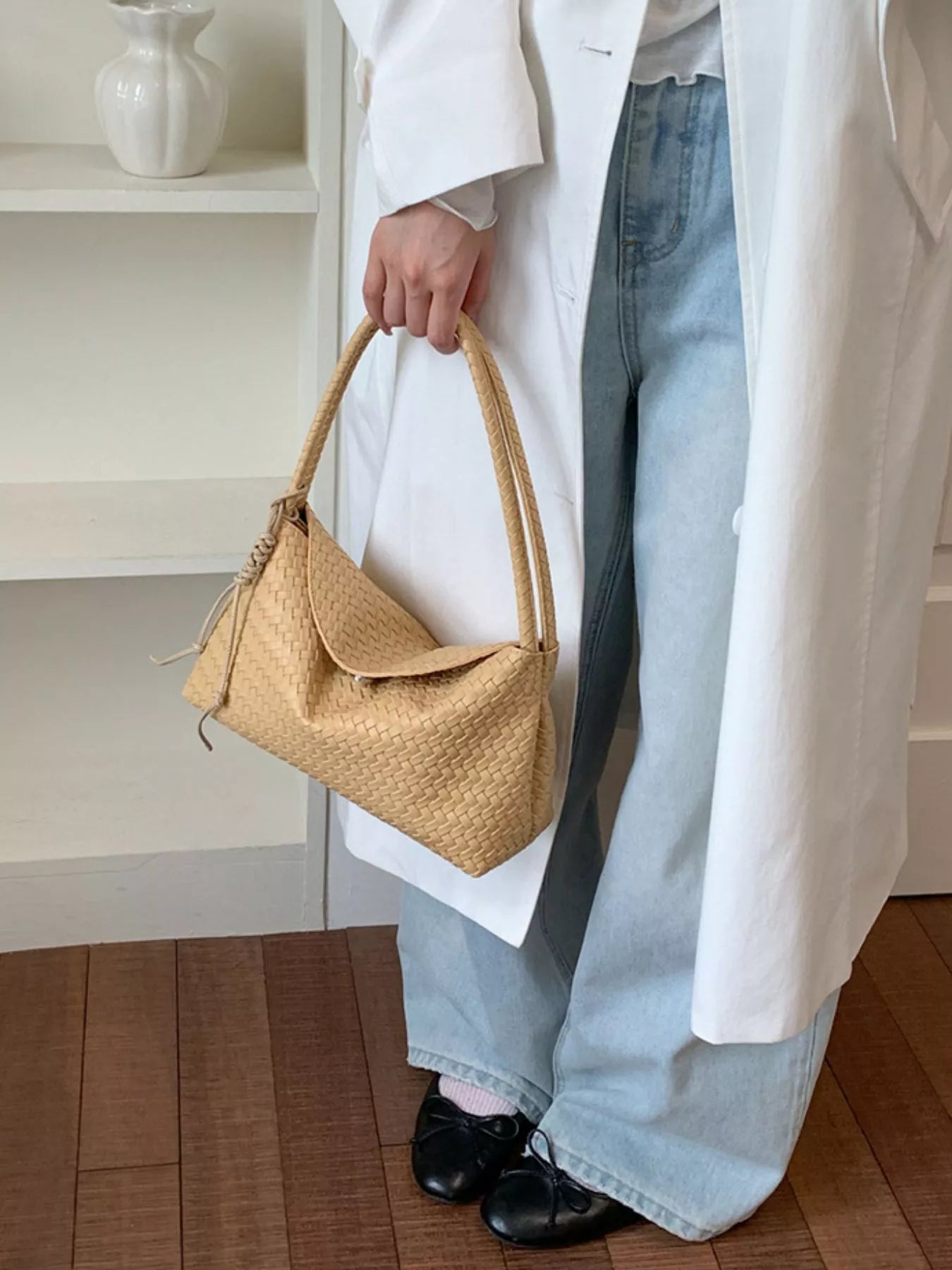 Beige woven vegan leather shoulder bag held at side, curved top and tied drawstring