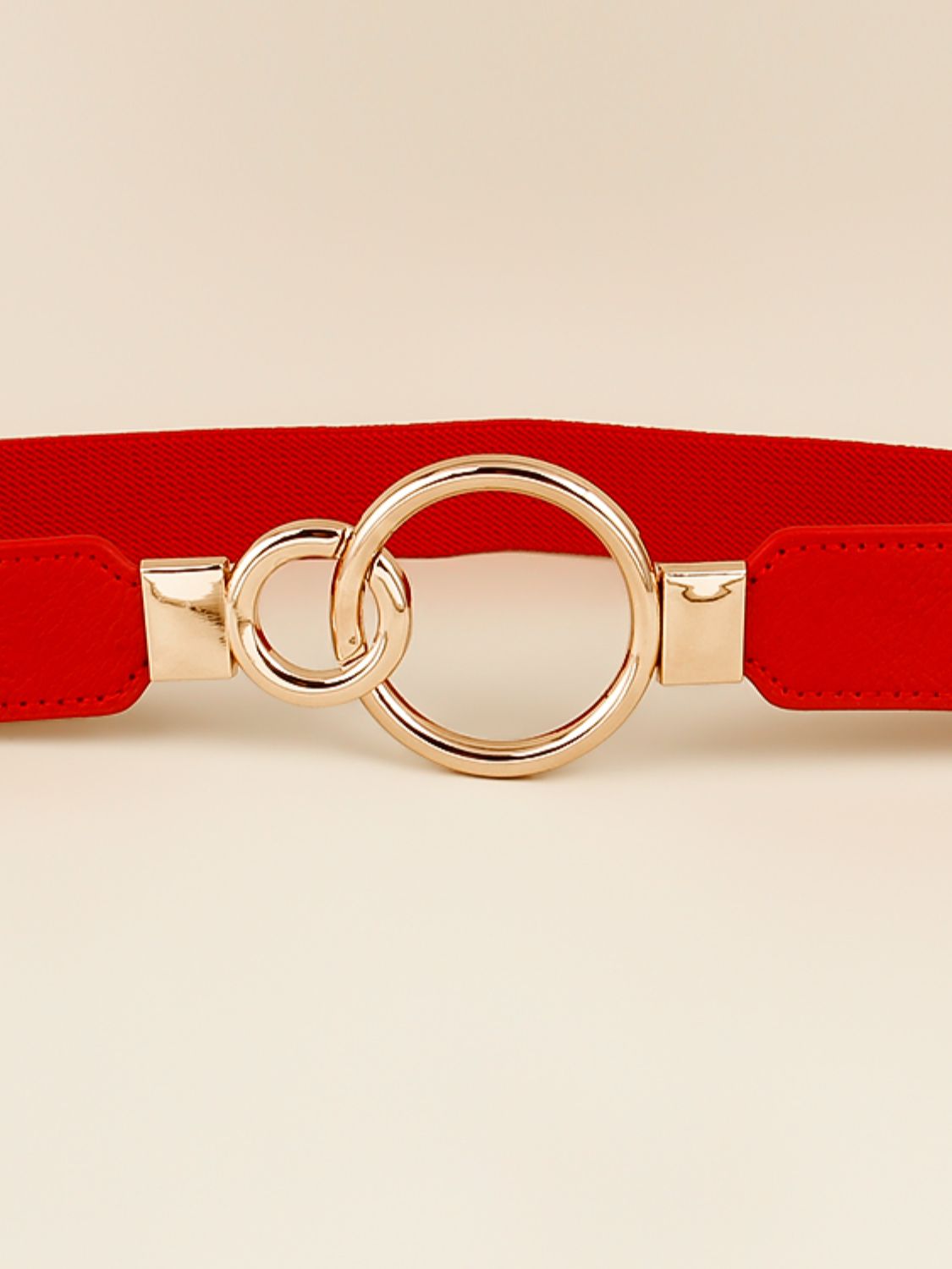 Red elastic belt close-up with double ring buckle and rose-gold metal tabs
