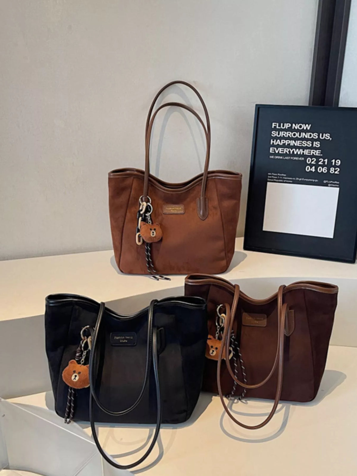 Brown suede tote bag with long handles, zipper top, and bear keychain charm