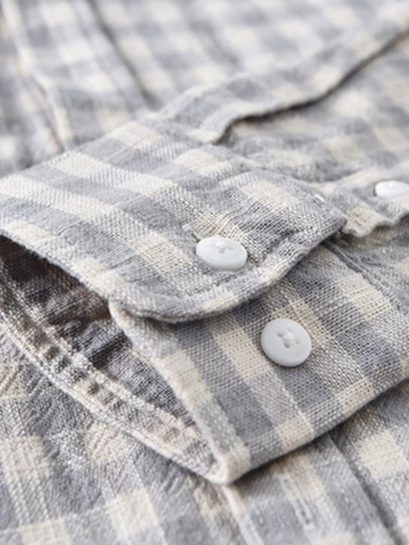 Gray plaid button-up shirt sleeve close-up with white buttons and cuff
