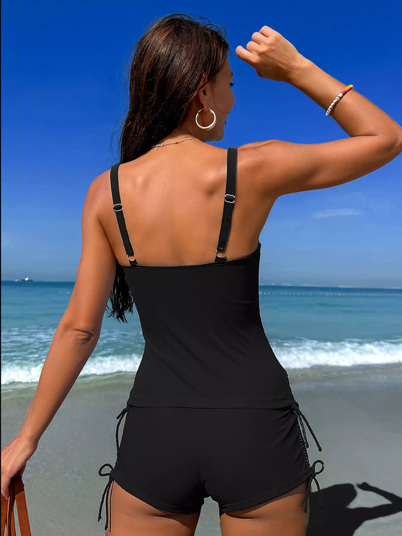 Black drawstring tankini set back view with adjustable straps on a sunny beach.