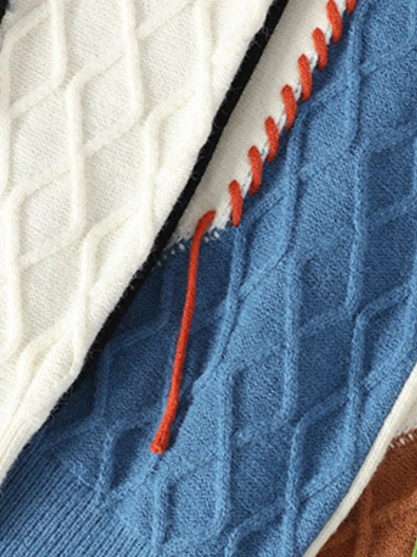 Cable knit sweater seam detail, blue knit with orange contrast stitching on cream trim