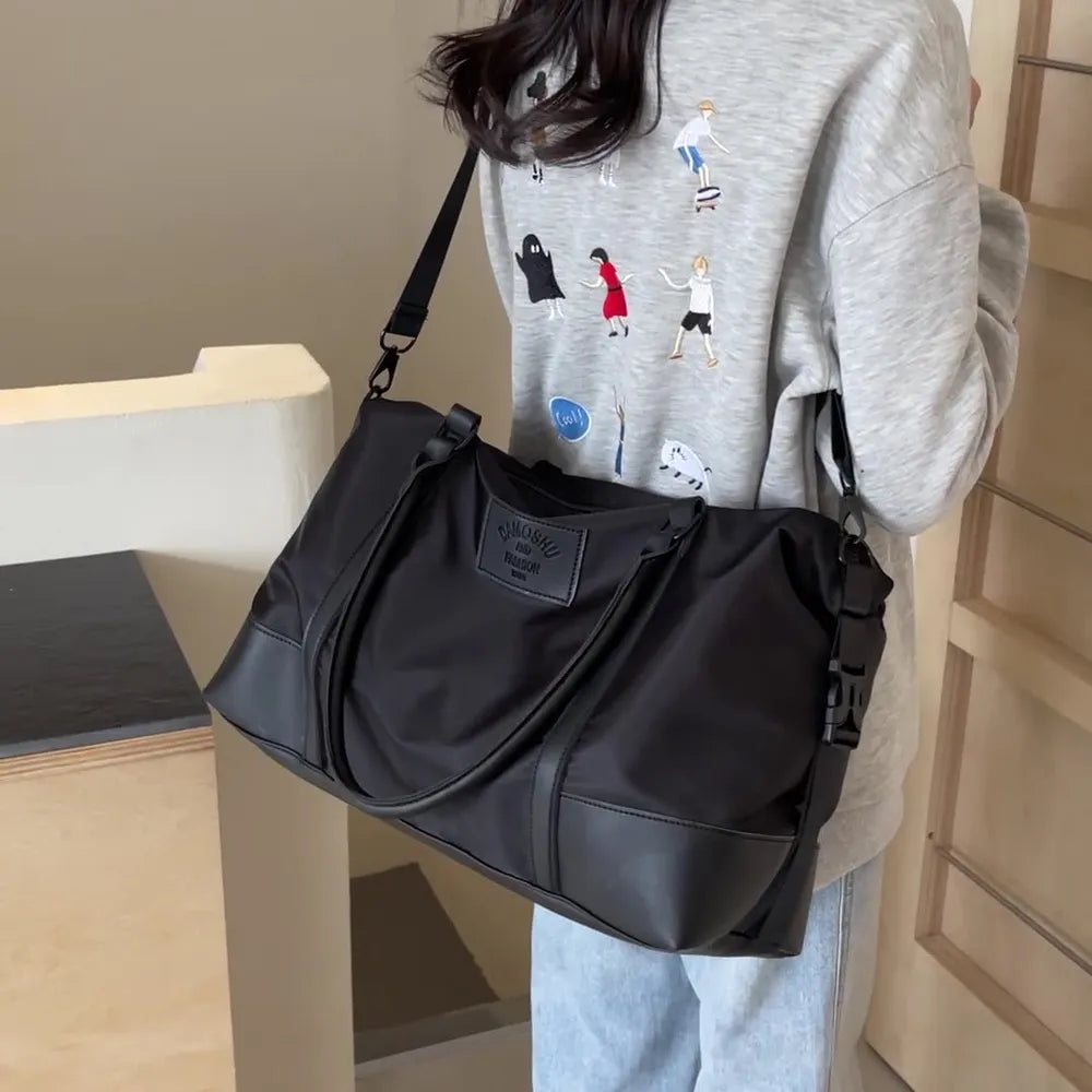 Black polyester travel duffel bag with detachable crossbody strap and front logo patch