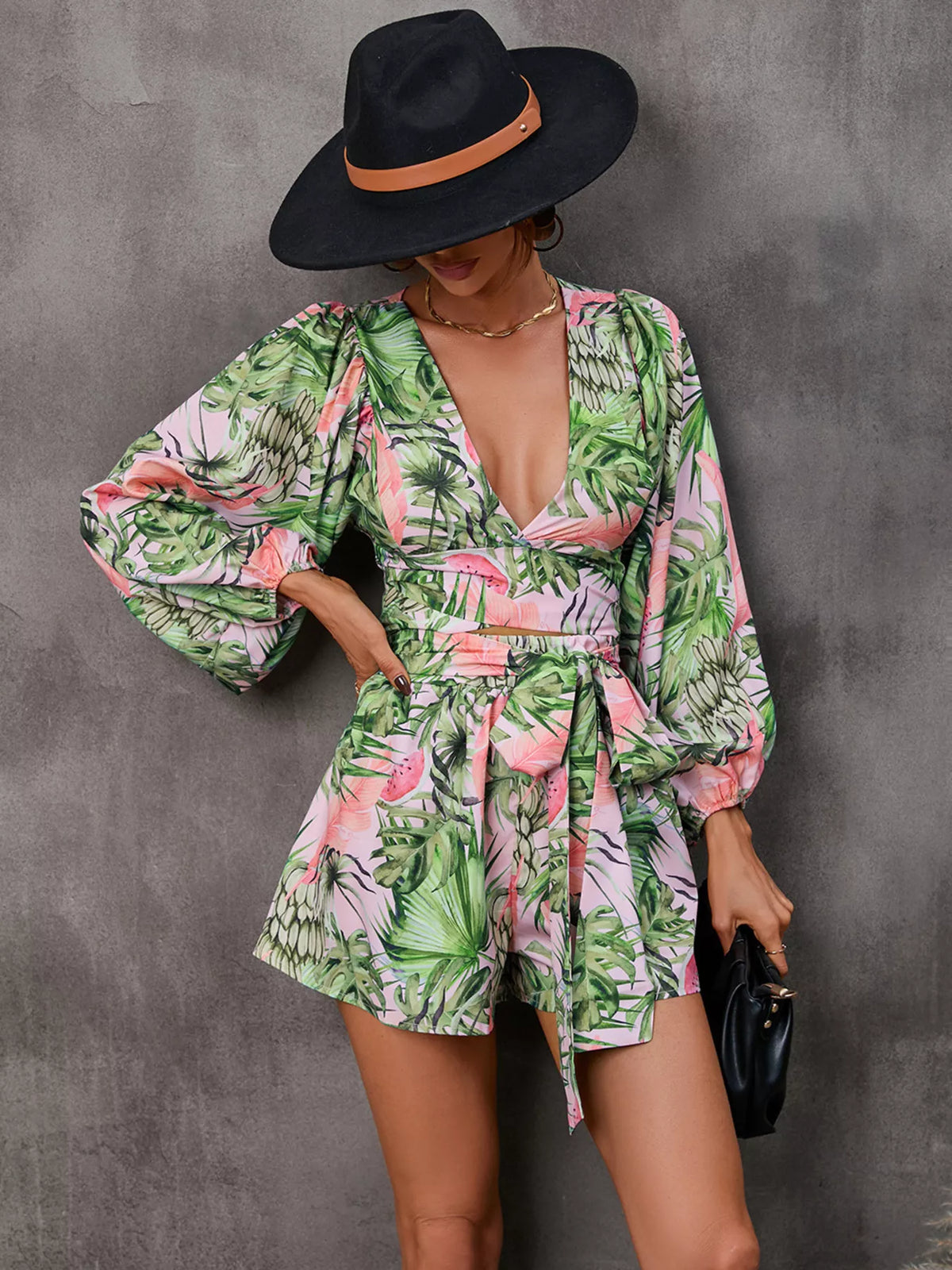 Printed long-sleeve romper with V-neck cutout and tied waist; green and pink tropical leaves