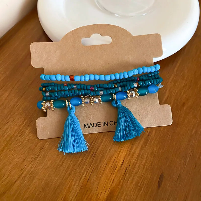 Blue beaded tassel bracelet with multiple strands, gold charms, and two blue tassels
