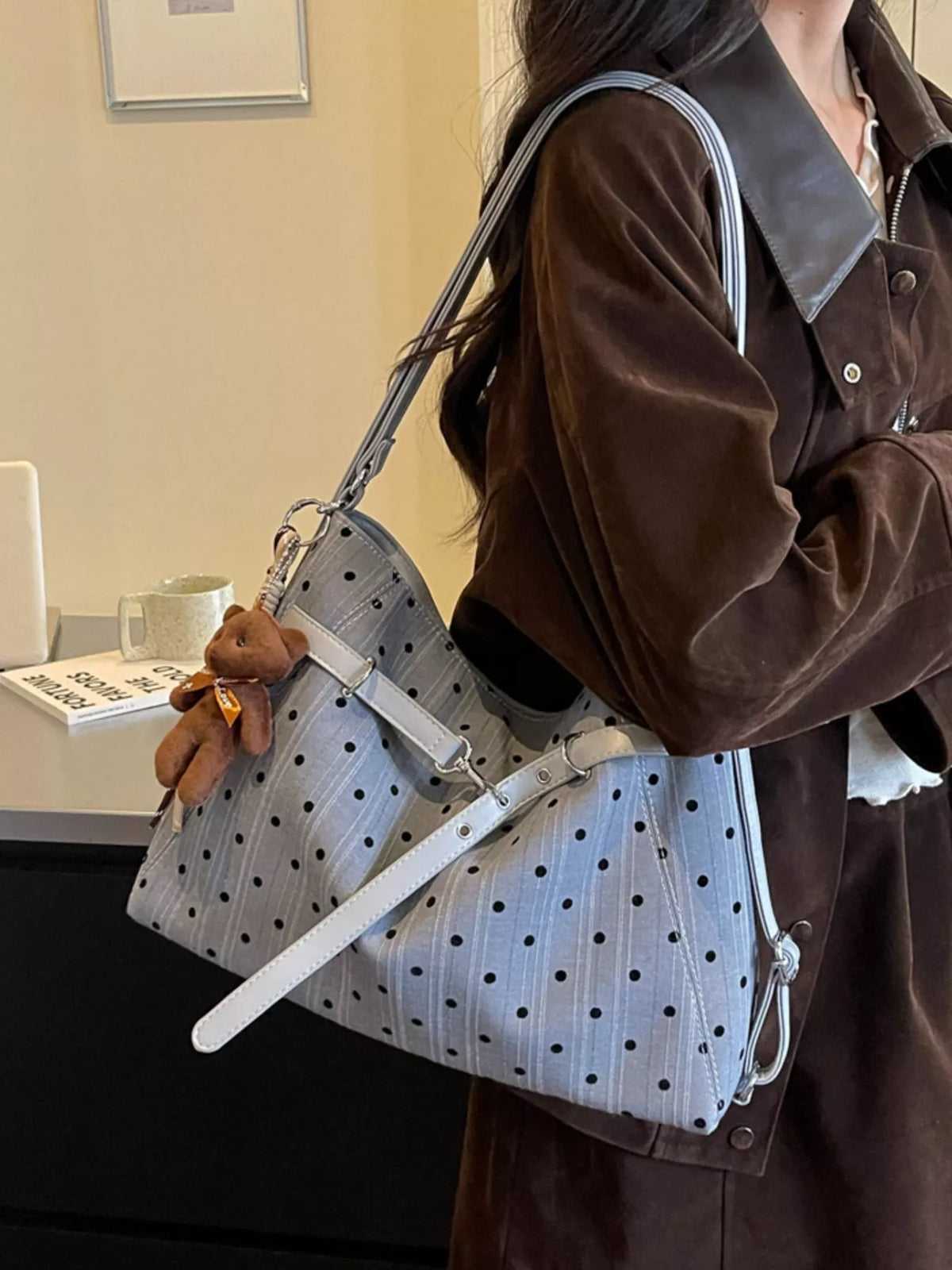 Light blue polka dot canvas shoulder bag with brown handles, buckles, and teddy keychain