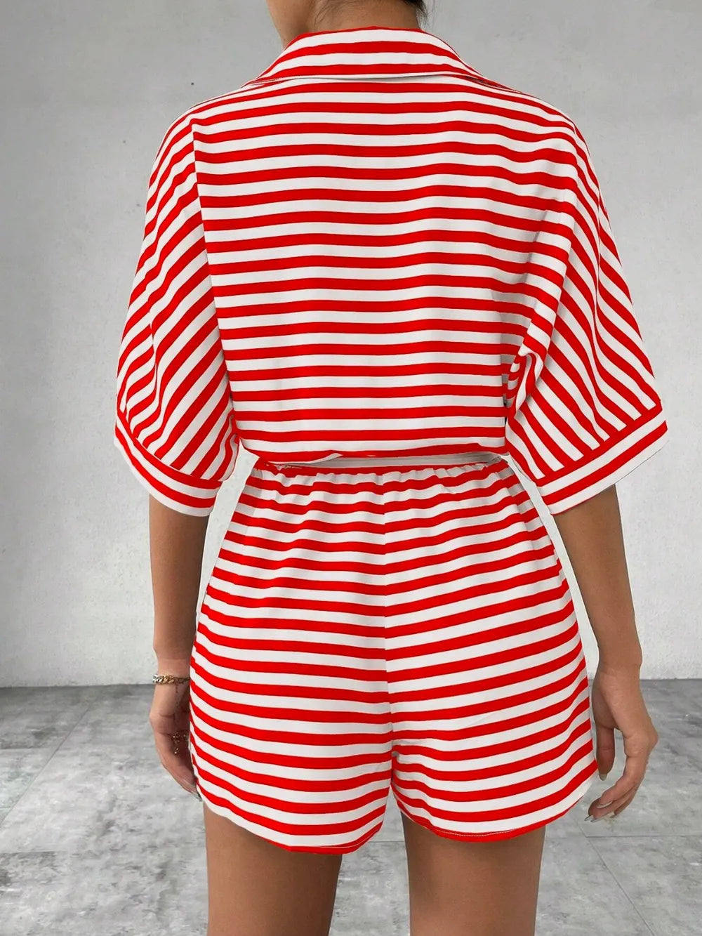 Back view of red and white striped button-front romper with tie waist and cuffed sleeves