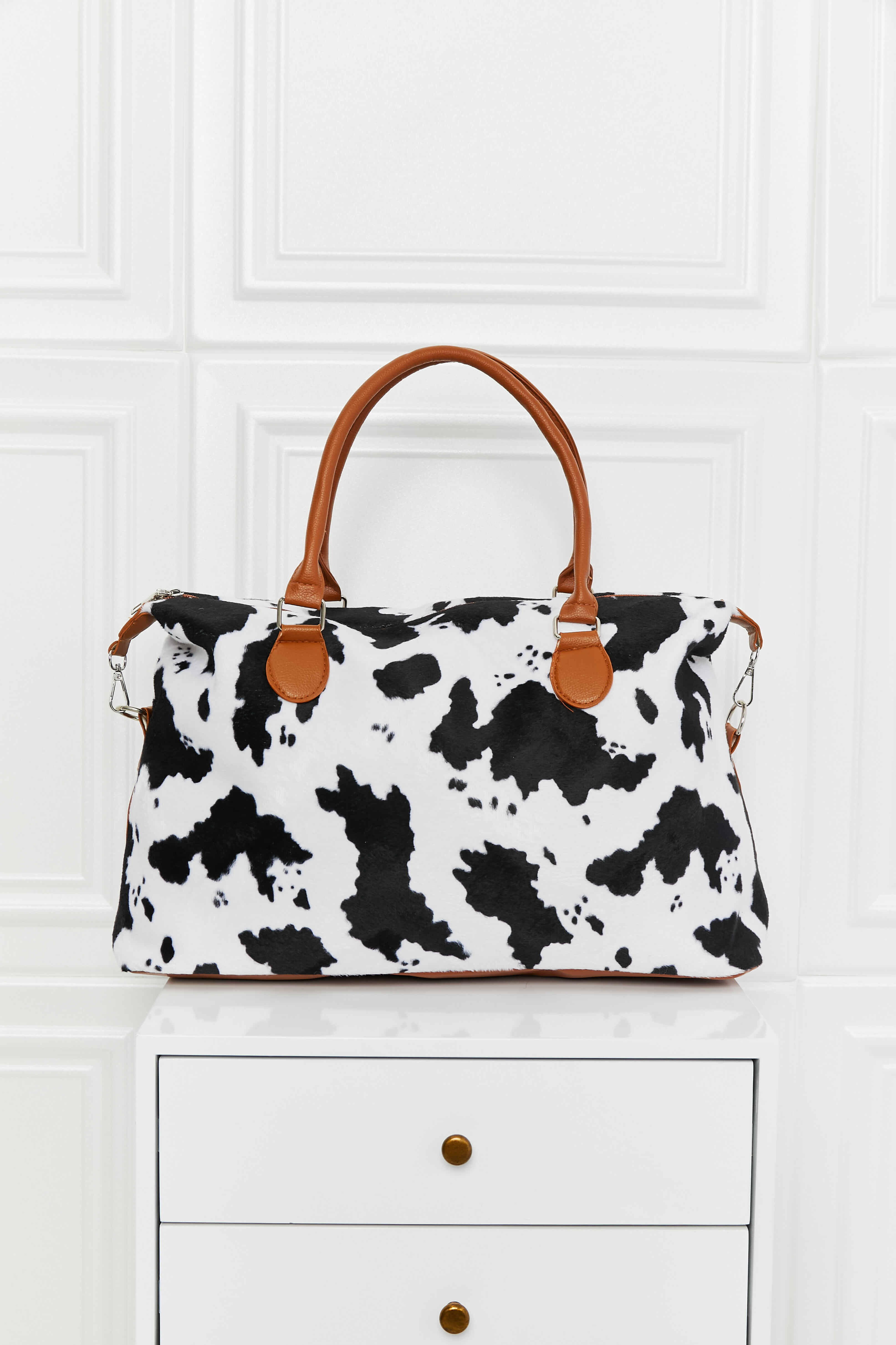Cow print weekender bag with brown handles, side clips, and front zipper