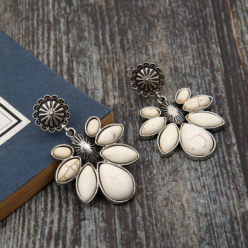White flower drop earrings with oval white petals, silver-tone sunburst discs, and hooks.