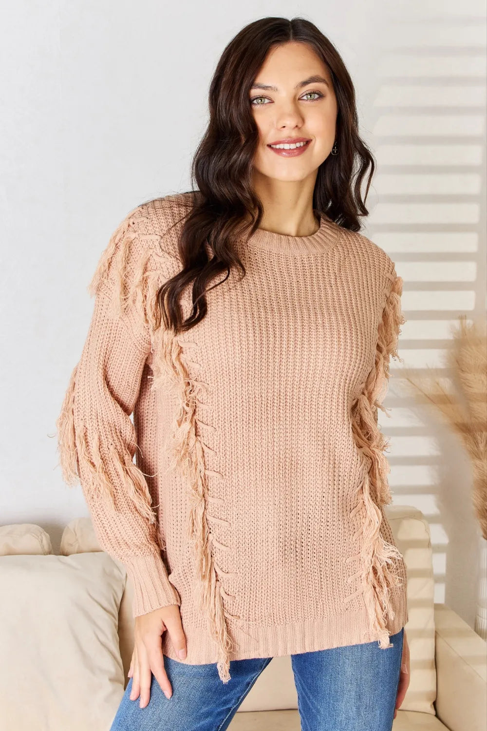 Dusty pink knit sweater with long sleeves and fringe tassel accents on shoulders