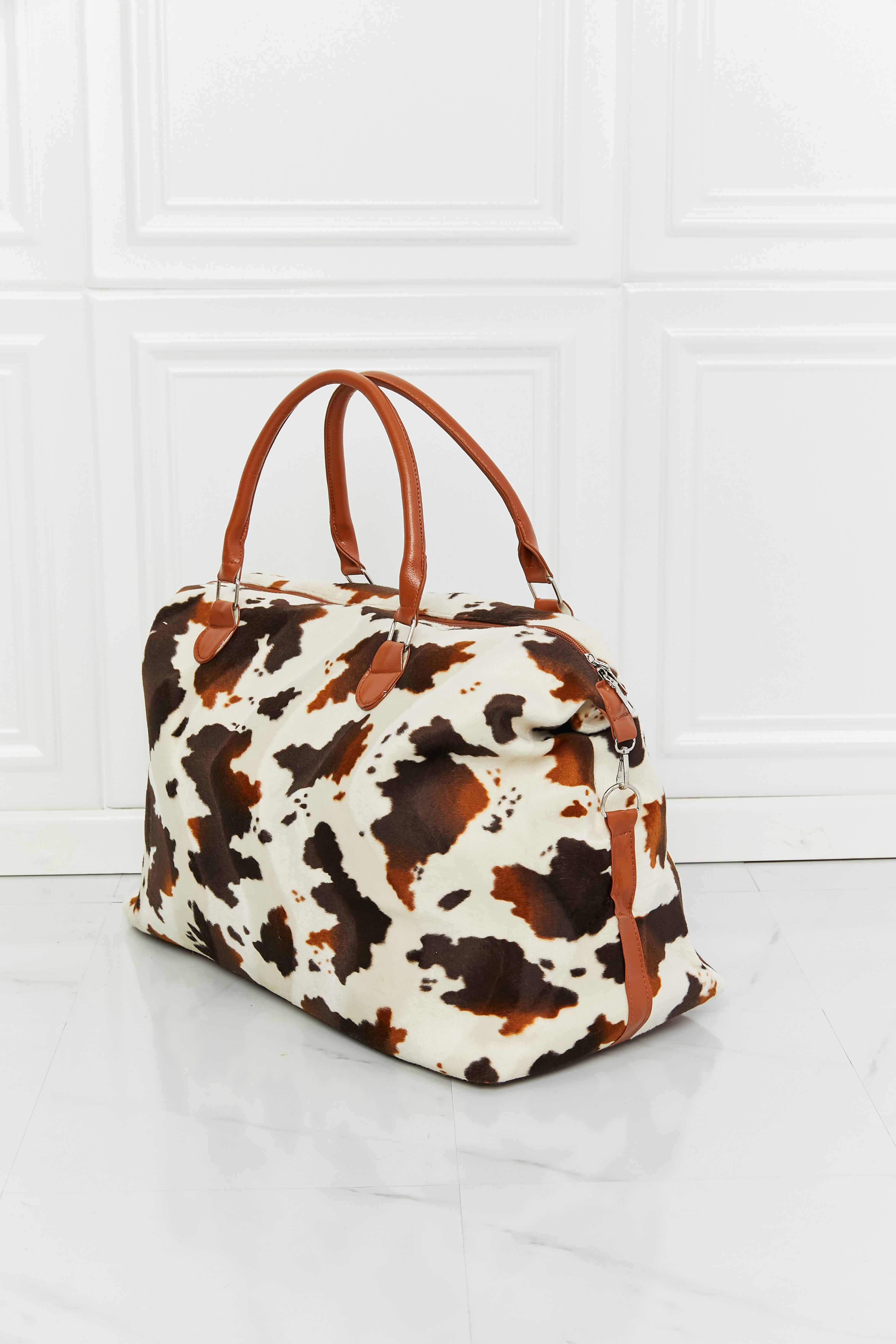 Cow print plush weekender bag with tan handles and zip-top in white and brown