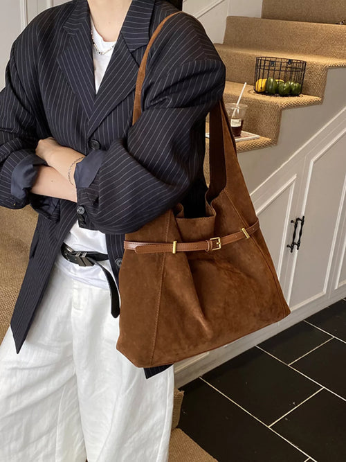 Brown suede bucket shoulder bag with wide adjustable strap and metal buckle closure.