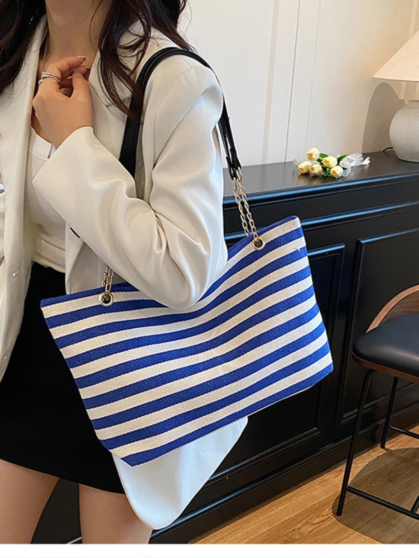 Blue and white striped tote shoulder bag with gold chain strap, worn over an outfit.