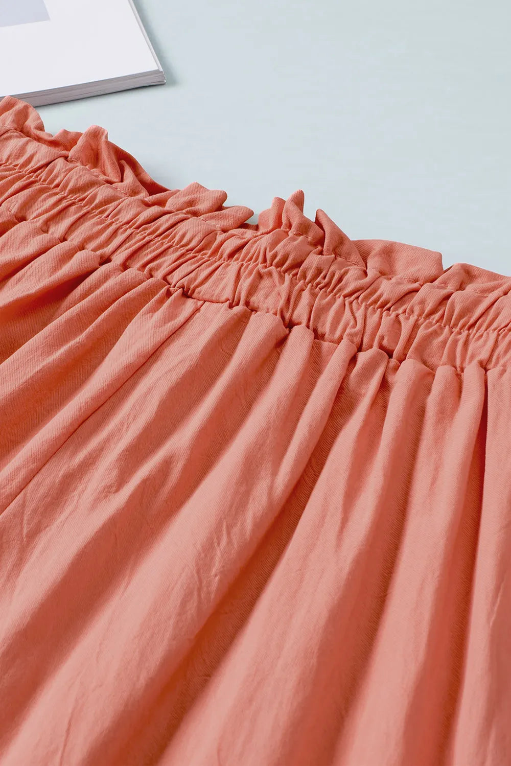 Coral paperbag waist wide-leg pants close-up with gathered waistband and vertical pleats.