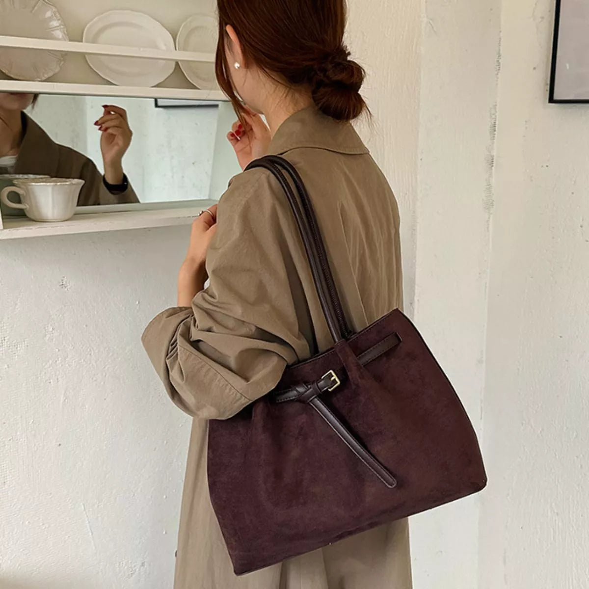 Dark brown suede shoulder bag worn crossbody, with front tab pocket and long strap
